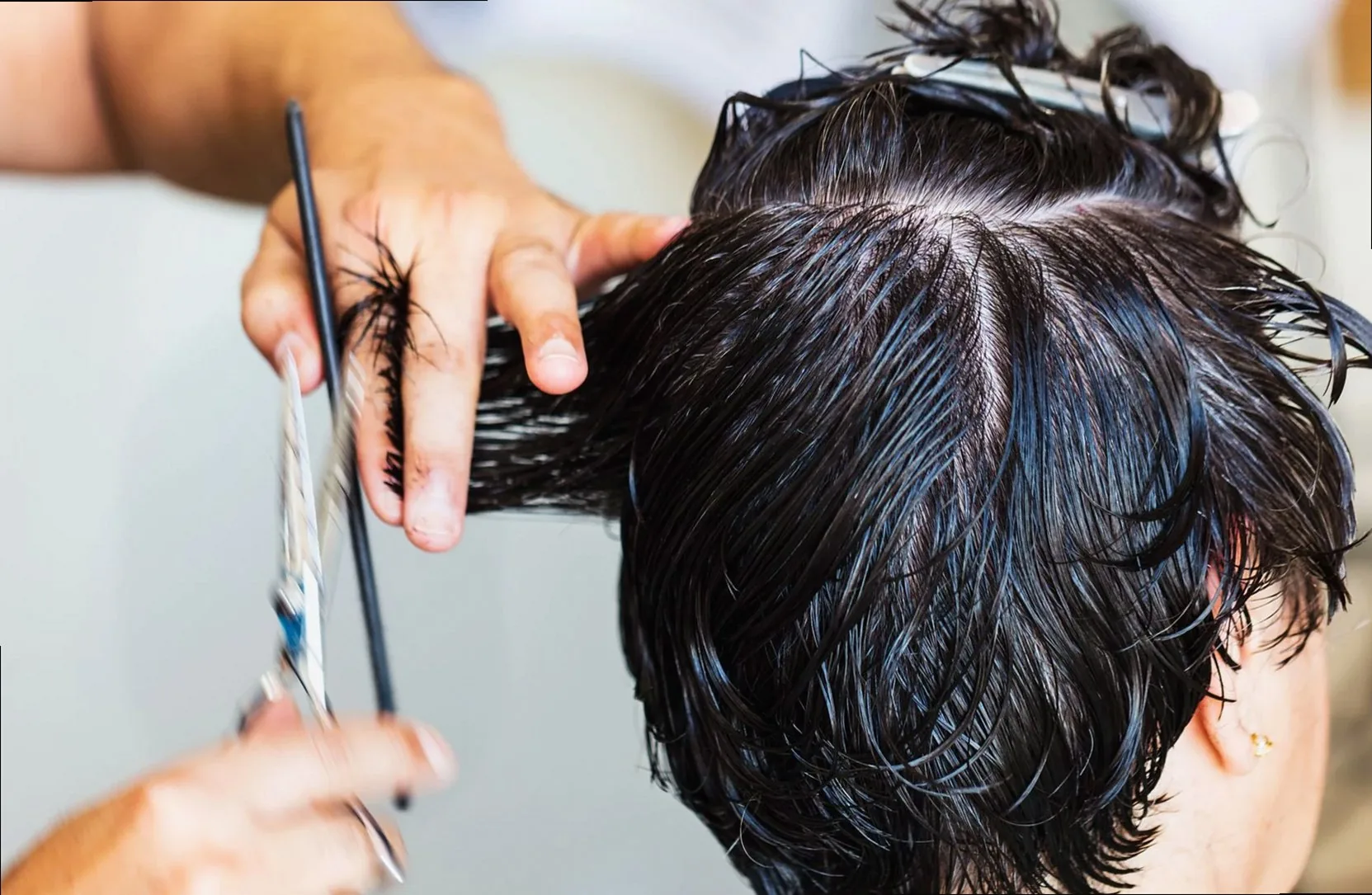 Close-up of a stylist cutting dark, wet hair in a salon setting, showcasing the precision and technique of hairstyling.